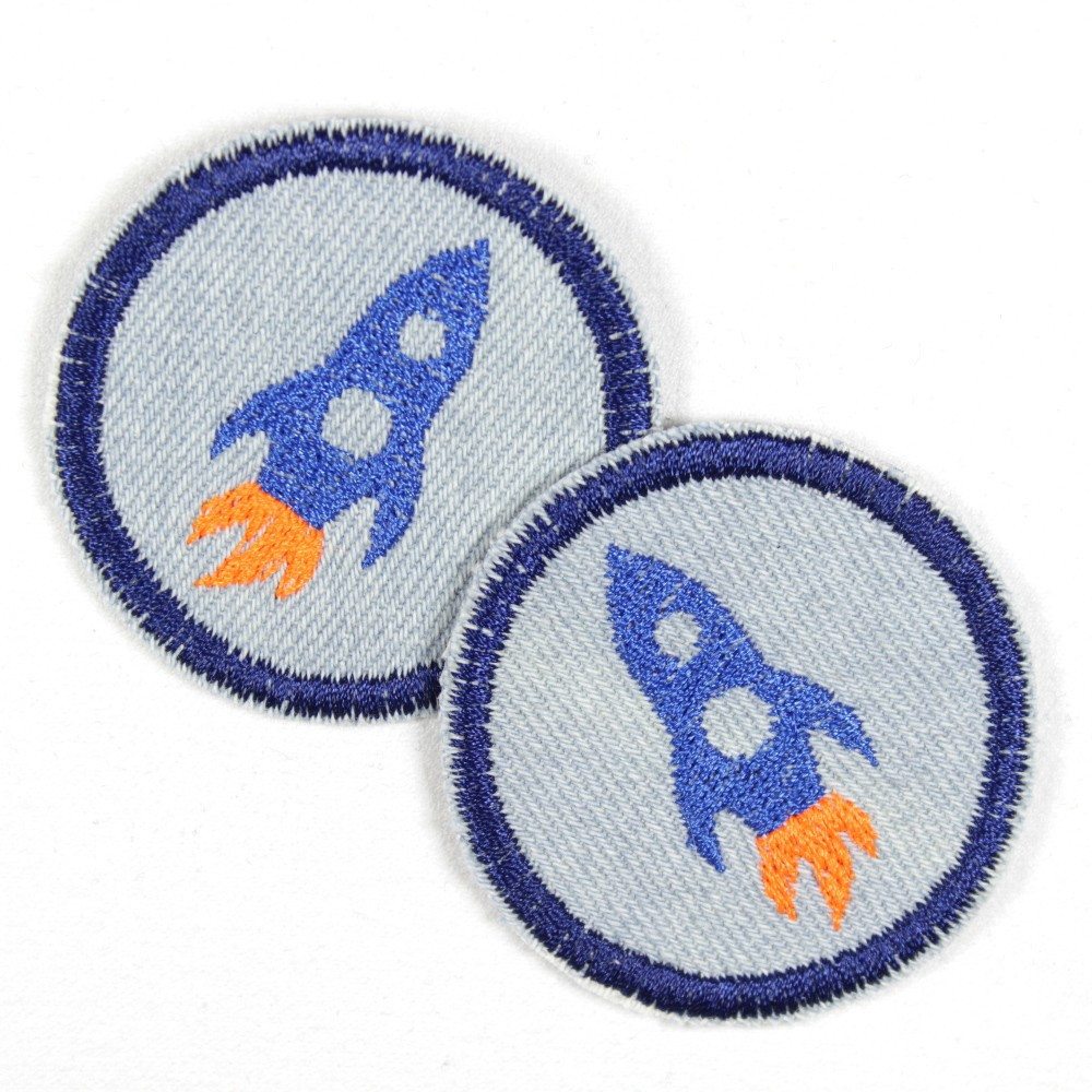 zwei kleine runde, hellblaue Flicken blau eingefasst und mit einer blauen Rakete, die von einem neon orangen Feuerstrahl angetrieben wird, bestickt
